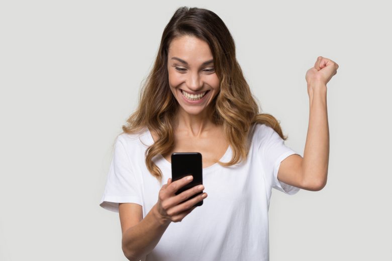 Happy excited woman celebrating success, online win, attractive female looking at phone screen, reading good news, satisfied client customer receive shopping offer, isolated on studio background