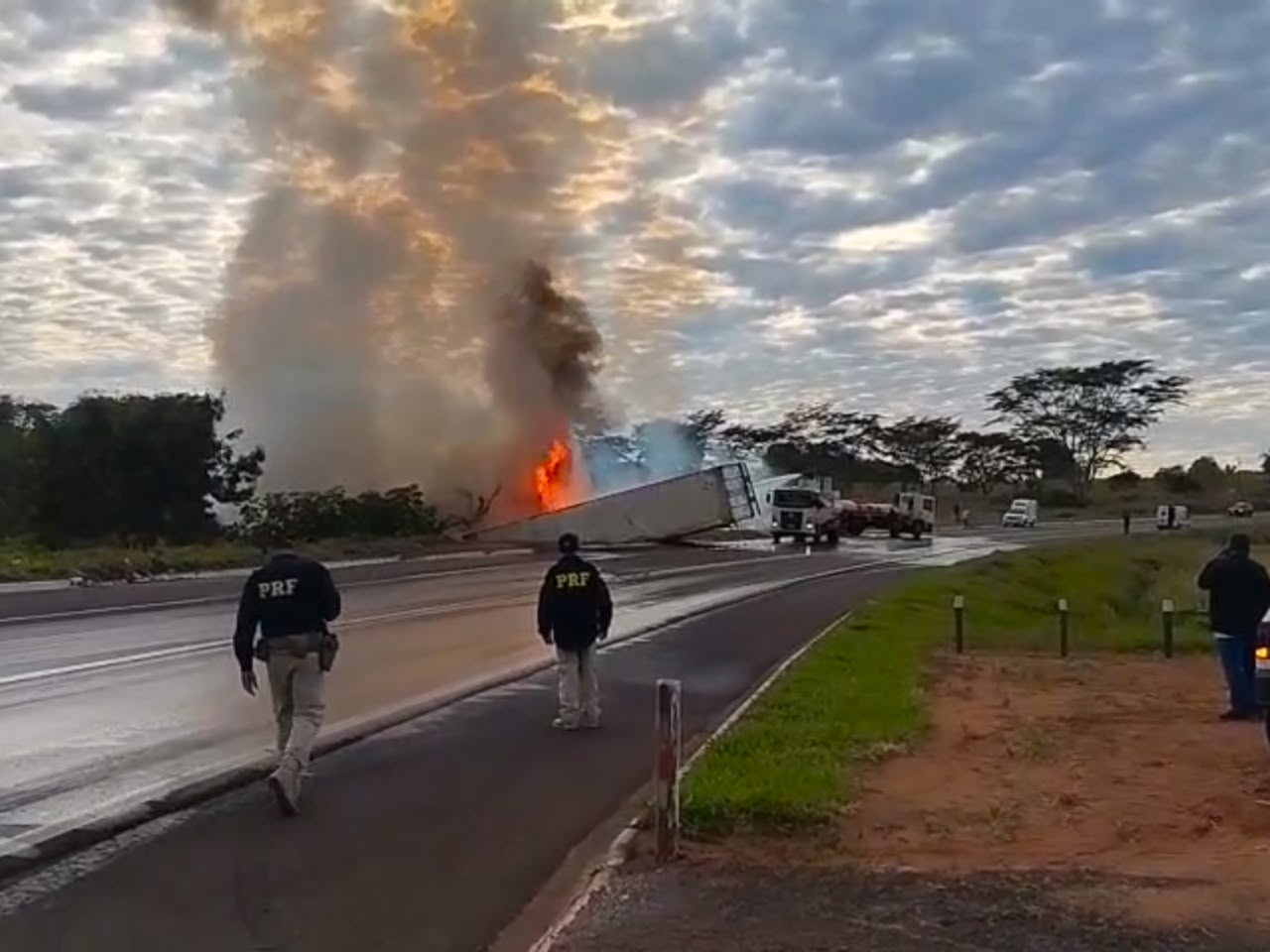 Equipes tentam controlar fogo após caminhão tombar. Condutor ficou preso às ferragens